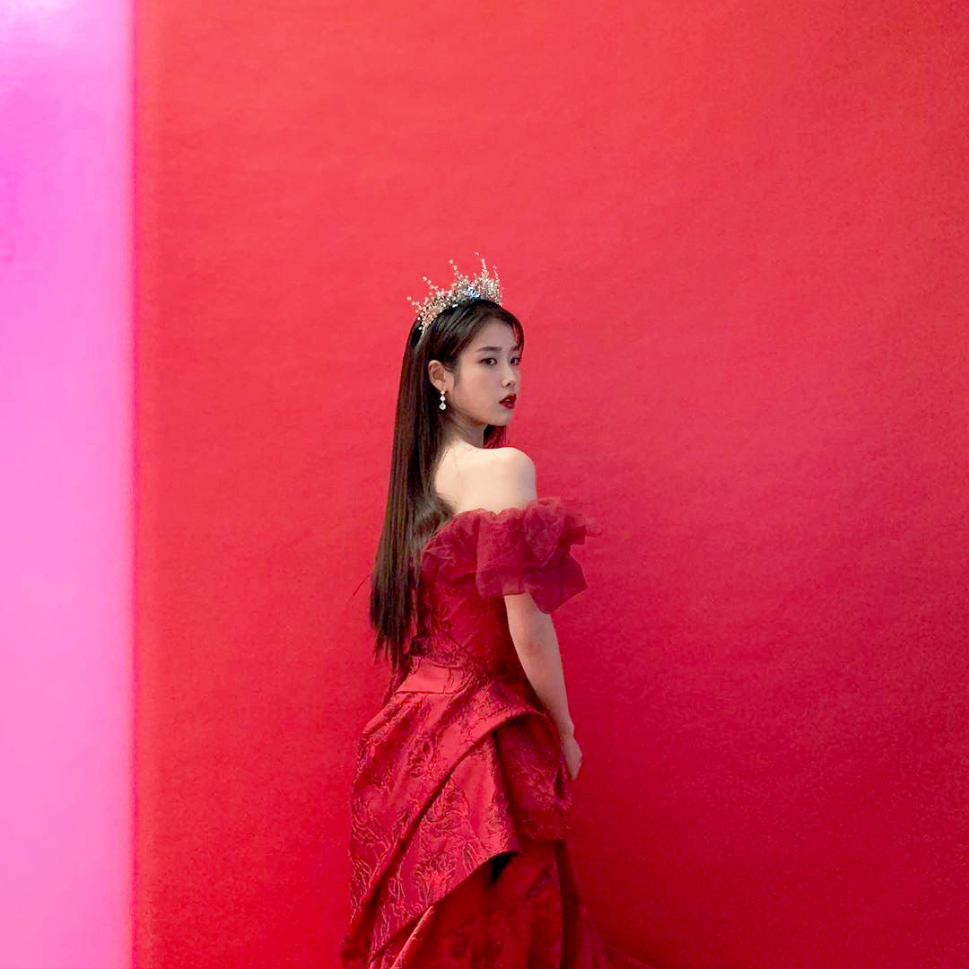 She wears a queen's dress and crown and. iu in red gown. 