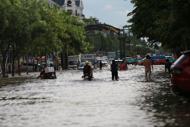 Trời hửng nắng, nhiều tuyến đường ở Hà Nội vẫn ngập sâu, người dân dùng tấm chắn để ngăn nước tràn vào nhà- Ảnh 1.