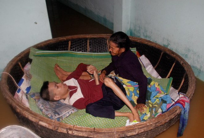 Quặn l&ograve;ng cảnh mẹ 72 tuổi neo th&uacute;ng giữ con chất độc da cam giữa lũ - Ảnh 1.