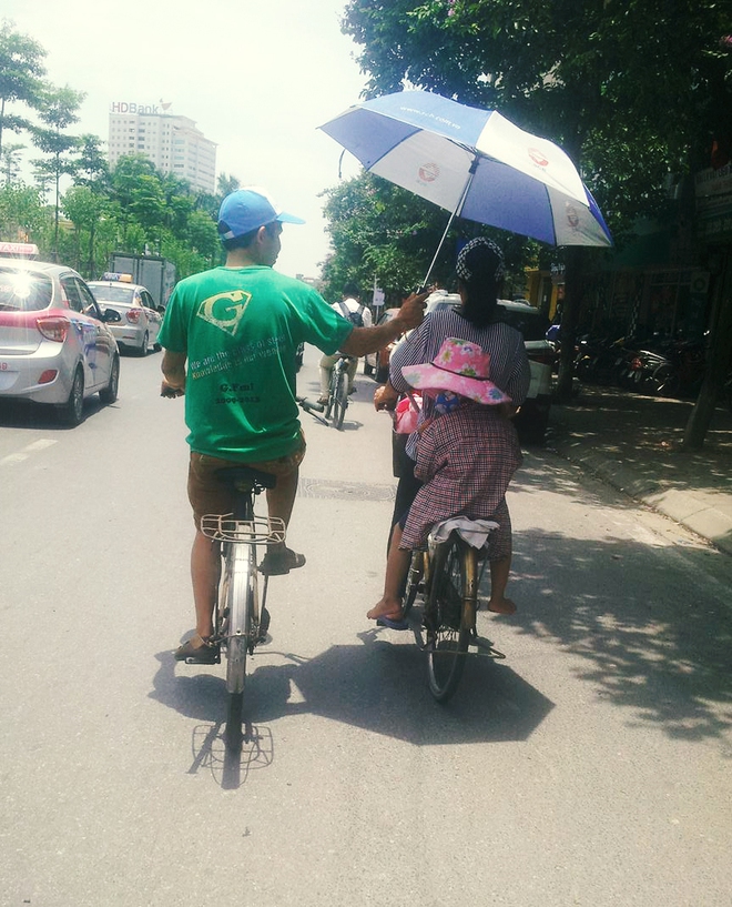 Hình ảnh dễ thương ngày Hà Nội nóng đỉnh điểm: Người đàn ông chạy xe đạp che ô cho hai mẹ con trên phố - Ảnh 1.